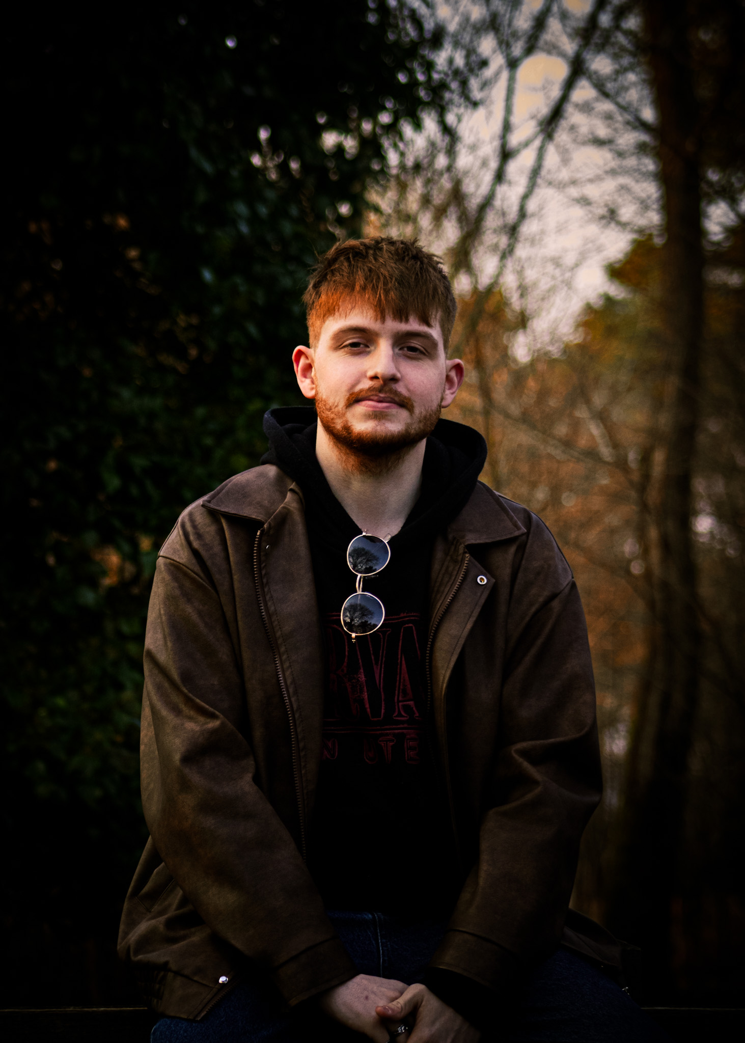 Portrait of a ginger bearded man in sunglasses and jacket. Moody outdoor setting.