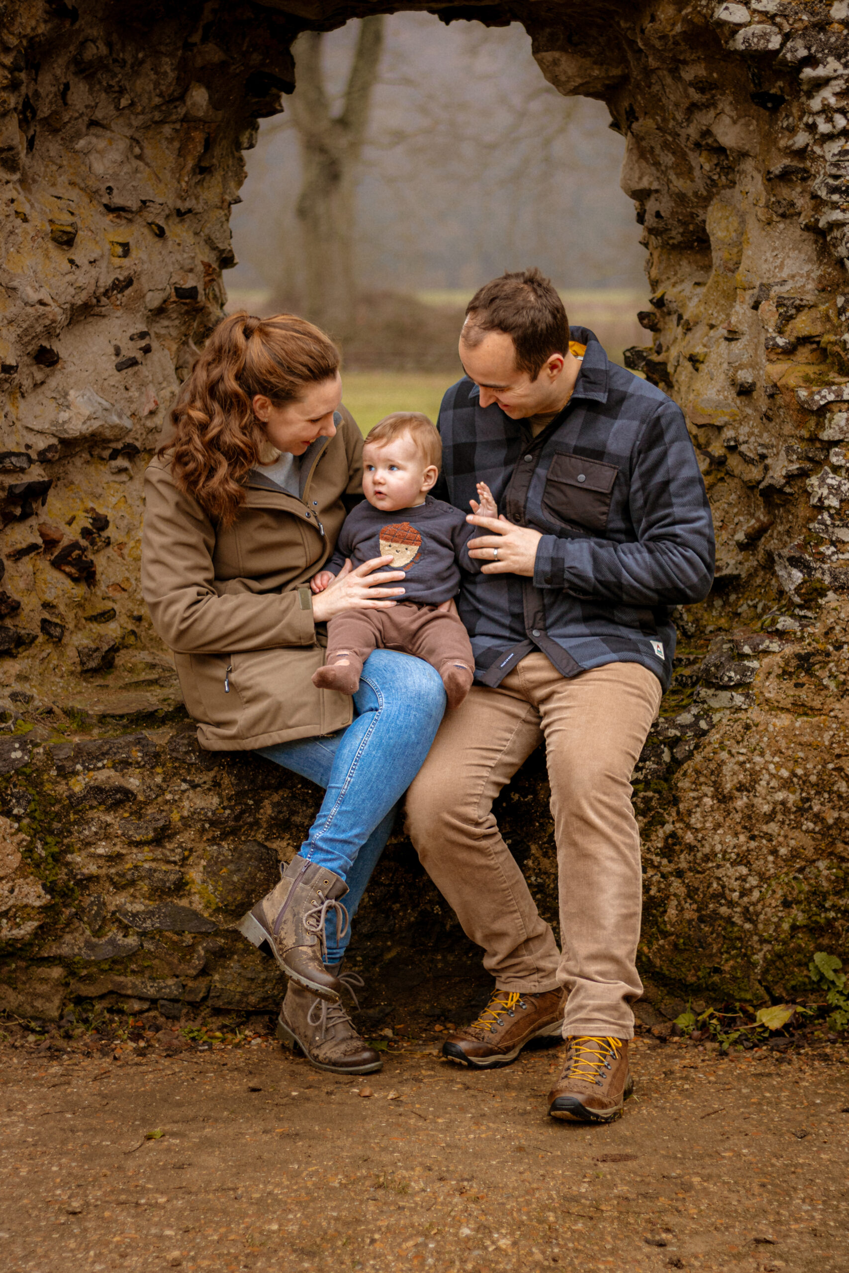 Natural family portrait in Petersfield under a stone arch. Candid photography session with parents and baby.